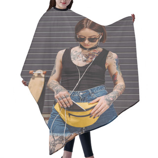 Personality  Stylish Tattooed Woman Listening Music In Earphones And Putting Smartphone In Waist Bag  Hair Cutting Cape
