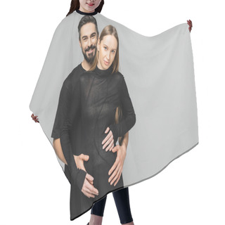 Personality  Positive And Bearded Man In Black T-shirt Hugging Fashionable And Pregnant Wife In Black Dress And Looking At Camera While Standing Isolated On Grey, Concept Of Birth Of Child Hair Cutting Cape