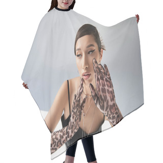 Personality  Stunning Asian Woman With Brunette Hair Posing In Trendy Spring Outfit With Hands Near Face On Grey Background With Lighting, Bold Makeup, Black Strap Dress, Animal Print Gloves, Generation Z Hair Cutting Cape