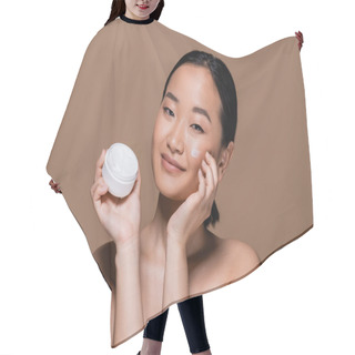 Personality  Pretty Asian Woman With Naked Shoulders Applying Cosmetic Cream On Cheek Isolated On Brown  Hair Cutting Cape
