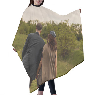 Personality  Back View Of Fashionable Couple In Newsboy Caps And Vintage Outfits Holding Hands And Walking Together On Blurred Field With Landscape At Background, Stylish Couple In Rural Setting Hair Cutting Cape