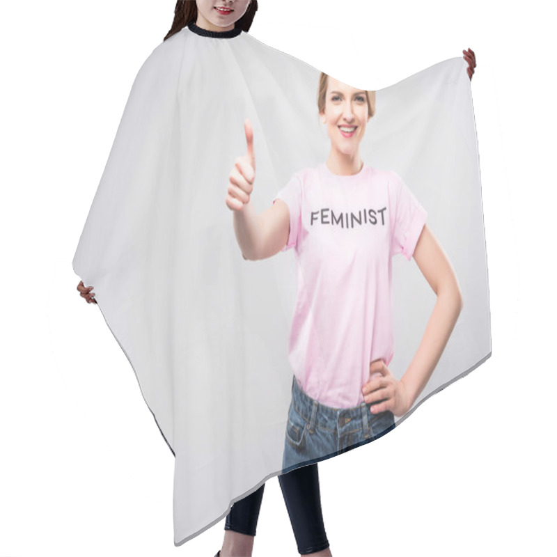 Personality  smiling woman in pink feminist t-shirt showing thumb up, isolated on grey hair cutting cape