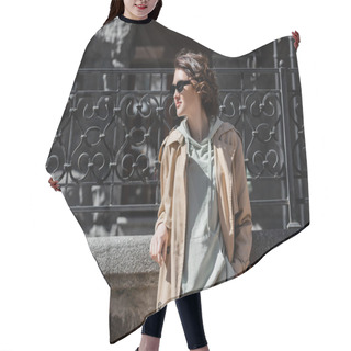 Personality  Travel Lifestyle, Young And Fashionable Woman With Wavy Brunette Hair, In Dark Sunglasses, Beige Trench Coat And Grey Hoodie Looking Away While Standing Near Forged Fence On City Street, Travel Lifestyle Hair Cutting Cape