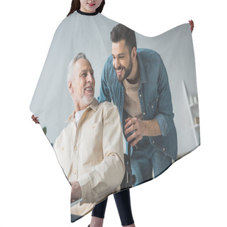 Personality  Cheerful Disabled Retired Man Sitting In Wheelchair Near Handsome Son Looking At Laptop Hair Cutting Cape