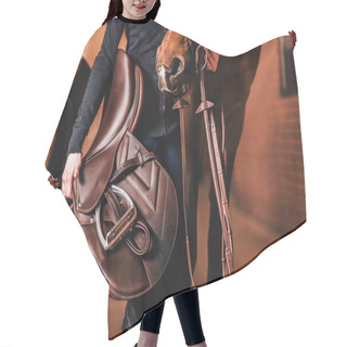 Personality  Unrecognizable Rider Standing Next To The Horse Inside Modern Red Brick Stable With Brown Leather Saddle In The Hand. Equestrian Lifestyle Theme. Hair Cutting Cape