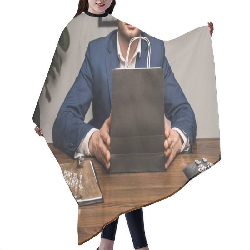 Personality  Cropped view of jewelry appraiser holding paper bag near jewelry on table in workshop hair cutting cape