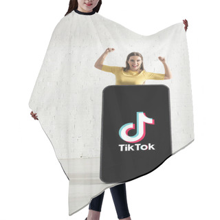 Personality  KYIV, UKRAINE - FEBRUARY 21, 2020: Cheerful Girl Showing Yeah Gesture While Standing Near Model Of Smartphone With TikTok App  Hair Cutting Cape