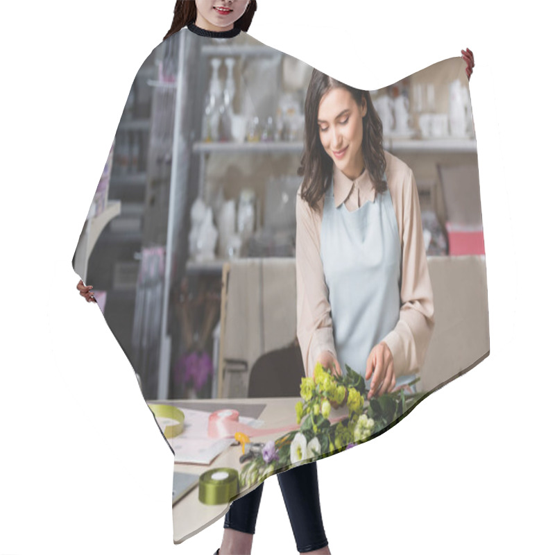 Personality  young florist making bouquet with eustoma flowers near laptop and racks on blurred background hair cutting cape