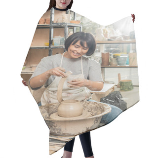 Personality  Cheerful Young Brunette Asian Artisan In Apron Holing Clay While Making Vase On Pottery Wheel Near Tools And Bowl In Blurred Ceramic Workshop, Artisanal Pottery Production And Process Hair Cutting Cape