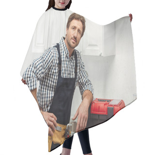 Personality  Handsome Workman In Tool Belt Looking At Camera Near Toolbox On Kitchen Worktop  Hair Cutting Cape