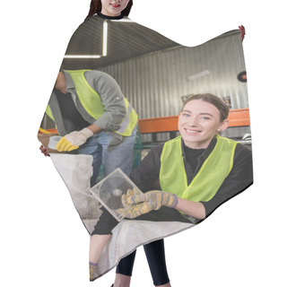 Personality  Smiling Young Worker In Reflective Vest And Gloves Looking At Camera While Holding Plastic Garbage For Recycle Near Sack And Blurred Indian Colleague In Waste Disposal Station, Garbage Sorting  Hair Cutting Cape