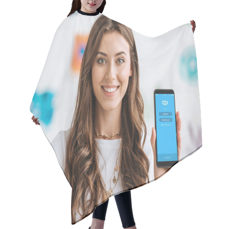 Personality  KYIV, UKRAINE - APRIL 17, 2019: Happy smiling girl showing smartphone with Skype app on screen and looking at camera. hair cutting cape