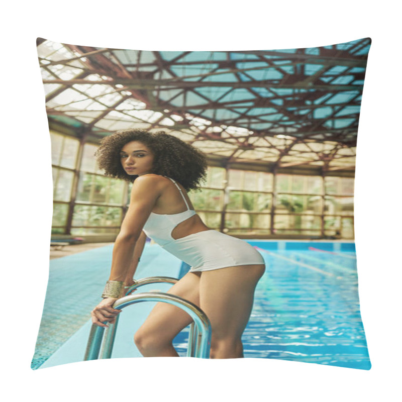 Personality  young and curly african american woman in bathing suit standing by pool ladder with blue water pillow covers