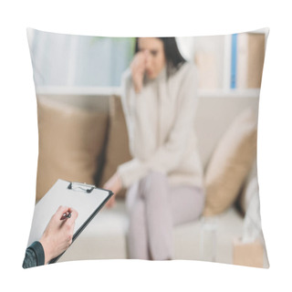Personality  Cropped Shot Of Psychotherapist Writing On Clipboard And Depressed Woman Sitting On Couch Behind Pillow Covers