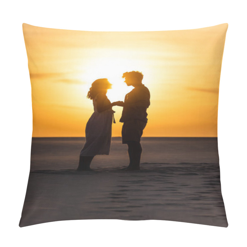 Personality  side view of silhouettes of man and woman holding hands on beach against sun during sunset pillow covers