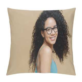 Personality  Magnetic Pretty Dark Skinned Woman Stands Sideways Indoor, Wears Dress, Shows Bare Shoulders, Smiles Gently, Has Curly Bushy Hair, Looks Through Optical Glasses At Camera, Isolated On Beige Wall Pillow Covers