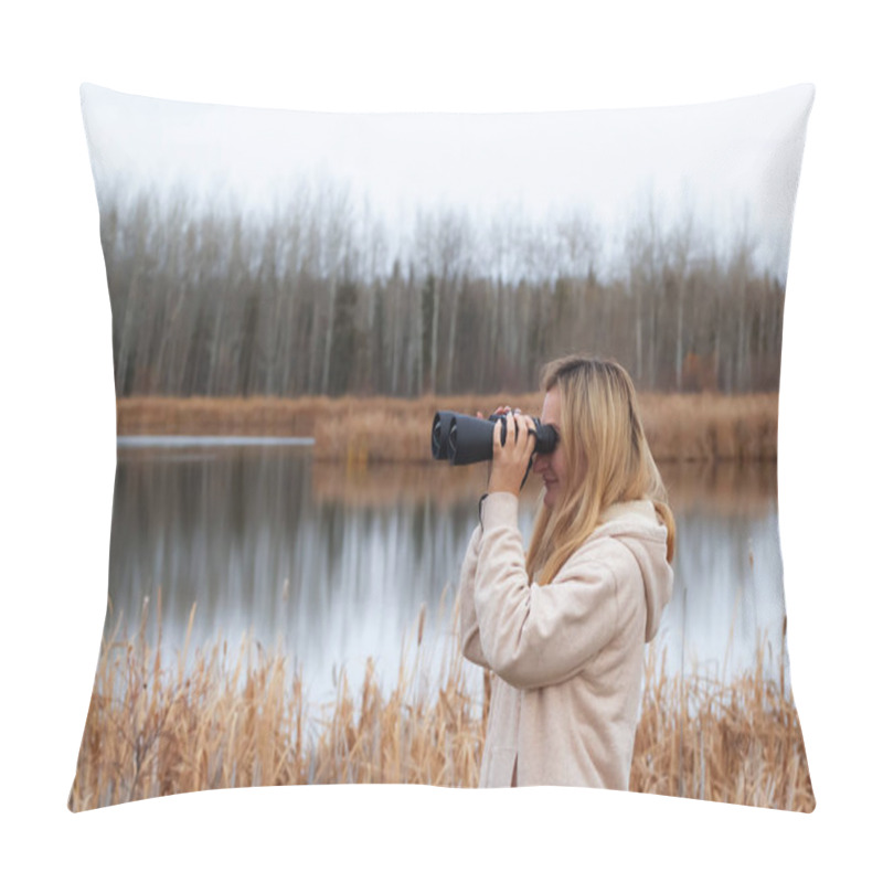 Personality  A blond caucasian woman in beige coat is watching through binoculars in the park near the lake in late autumn. pillow covers