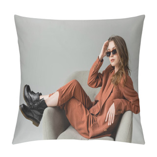 Personality  Stylish Young Woman With Long Hair Wearing Terracotta Suit With Blazer, Pants And Black Boots Posing In Trendy Sunglasses While Sitting In Armchair On Grey Background, Fashionable Model, Looking At Camera Pillow Covers
