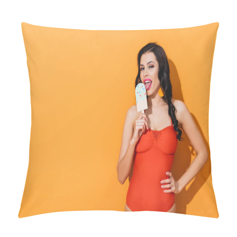 Personality  cheerful young woman licking paper cut ice cream and standing with hand on hip on orange  pillow covers