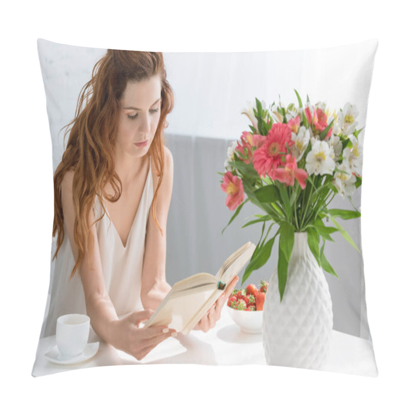 Personality  concentrated young woman reading book while sitting at table with coffee cup and flowers in vase pillow covers
