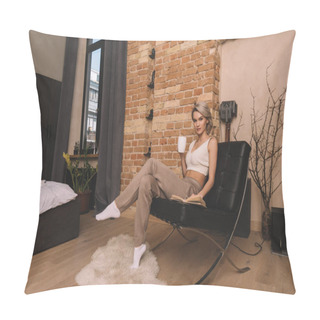 Personality  Attractive Woman Holding Cup Of Tea And Looking At Camera While Sitting In Armchair Near Book At Home Pillow Covers