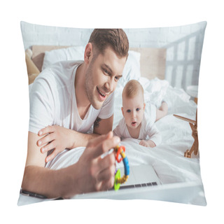 Personality  Selective Focus Of Smiling Father Showing Baby Rattle To Cute Little Son While Lying On Bed Near Laptop Pillow Covers