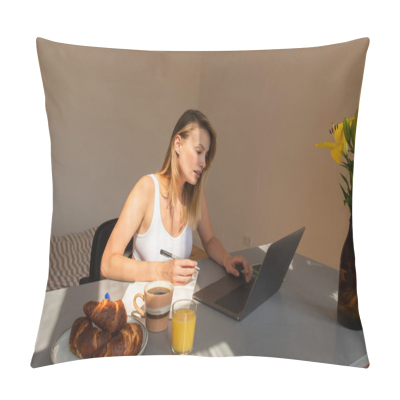 Personality  Young freelancer using laptop and notebook near breakfast with drinks at home  pillow covers