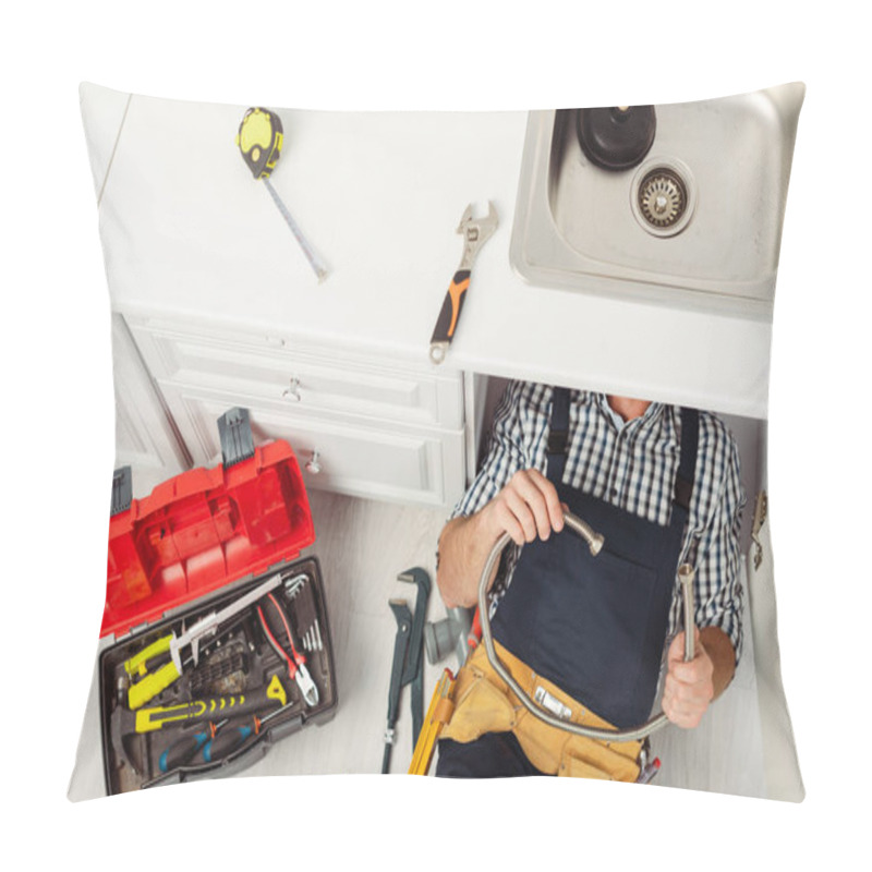 Personality  Top view of plumber holding metal pipe while repairing kitchen sink near tools on worktop and floor  pillow covers