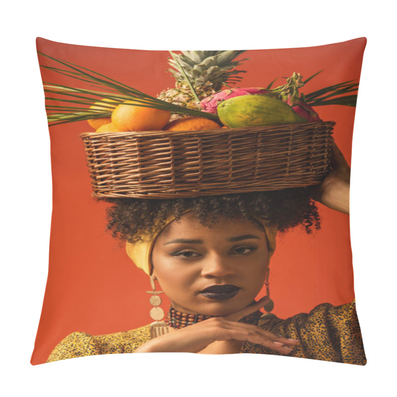 Personality  portrait of serious young african american woman holding basket with exotic fruits on head on red pillow covers