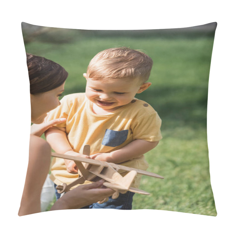 Personality  blurred cheerful mother near smiling toddler boy with wooden biplane  pillow covers