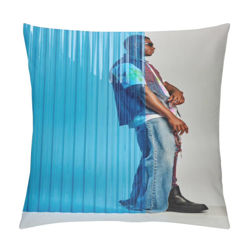 Personality  Side view of stylish afroamerican male model in ripped jeans, denim vest and sunglasses standing behind blue polycarbonate sheet on grey background, DIY clothing, sustainable lifestyle  pillow covers