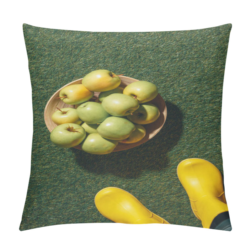Personality  cropped view of person in yellow rubber boots standing near wooden bowl with apples on green grass pillow covers