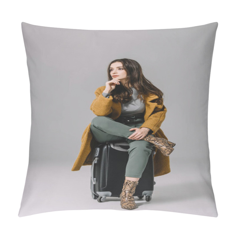 Personality  beautiful pensive woman in beige coat sitting on travel bag on grey pillow covers