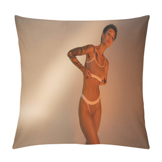Personality  Young Tattooed Woman With Slender Body Adjusting Bra And Looking At Camera On Beige Background Pillow Covers