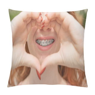 Personality  Close-up Portrait Of A Young Red-haired Woman With Braces On Her Teeth Holding Her Hands In The Shape Of A Heart. Orthodontic Appliances For A Perfect Smile. Pillow Covers