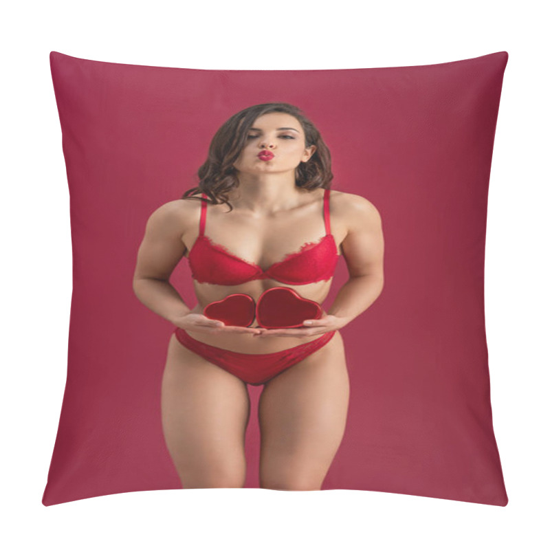 Personality  seductive girl in lingerie sending air kiss while holding heart-shaped gift boxes isolated on red pillow covers