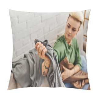Personality  Young Tattooed Woman Sitting On Couch In Living Room And Holding Grey Pants While Reducing Wardrobe Items At Home, Trendy Hairstyle, Tattoo, Sustainable Living And Mindful Consumerism Concept Pillow Covers