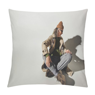 Personality  Full Length Of Trendy Hipster Style Man In Beanie Hat, Dark Sunglasses, Beige Trench Coat And Sneakers Looking At Own Shadow While Sitting With Crossed Legs On Grey Background With Copy Space Pillow Covers