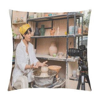 Personality  Asian Female Artisan In Headscarf And Workwear Talking At Digital Camera On Tripod While Working With Wet Clay On Pottery Wheel Near Rack In Art Workshop, Clay Sculpting Process Concept Pillow Covers