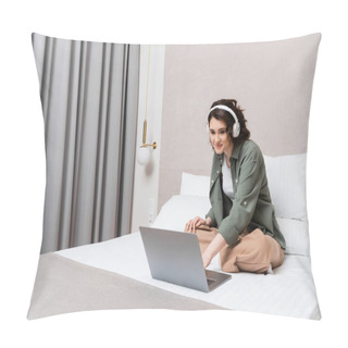 Personality  Happy Young Woman In Casual Clothes And Wireless Headphones Sitting On Bed Near White Pillows, Grey Curtains And Wall Sconce While Watching Movie On Laptop In Hotel Room, Leisure And Travel Pillow Covers