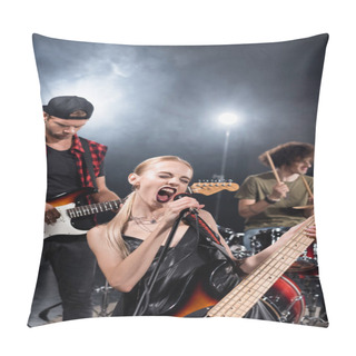 Personality  KYIV, UKRAINE - AUGUST 25, 2020: Female Vocalist Of Rock Band Shouting In Microphone Near Guitarist With Backlit And Blurred Drummer On Background Pillow Covers