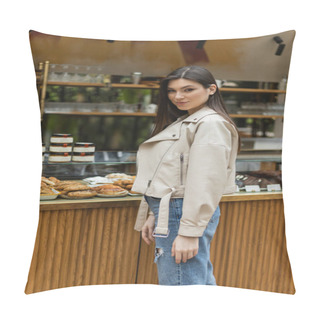 Personality  Brunette Young Woman With Long Hair In Beige Leather Jacket And Denim Jeans Looking At Camera While Standing Near Cake Display With Tasty Pastry And Jars Of Jam In Modern Bakery Shop In Istanbul  Pillow Covers