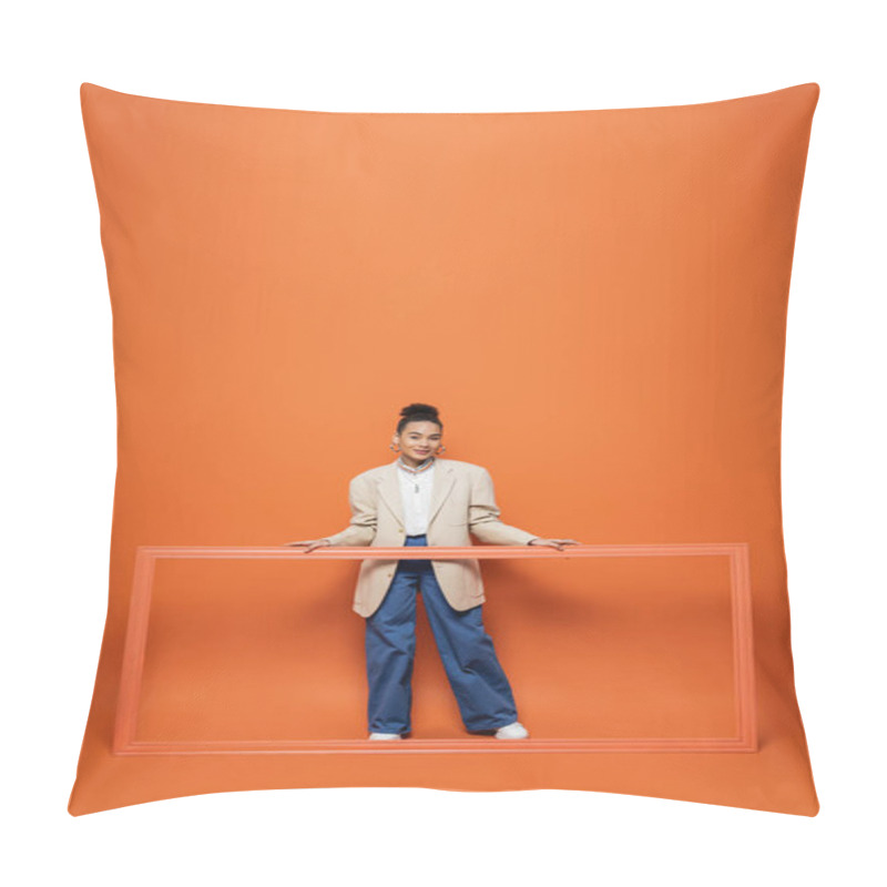 Personality  smiling african american model in beige blazer and blue pants holding frame on orange backdrop pillow covers