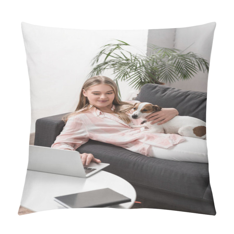 Personality  cheerful woman lying on couch with jack russell dog and using laptop in living room  pillow covers