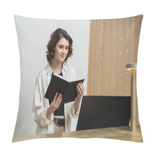 Personality  Positive Receptionist In Trendy Casual Clothes, With Wavy Brunette Hair Standing With Notebook Near Computer Monitor And Lamp On Front Desk In Lobby Of Contemporary Hotel  Pillow Covers