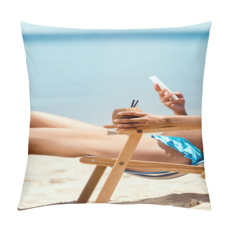 Personality  cropped image of woman holding cocktail in coconut shell and using smartphone while laying on deck chair on sandy beach  pillow covers
