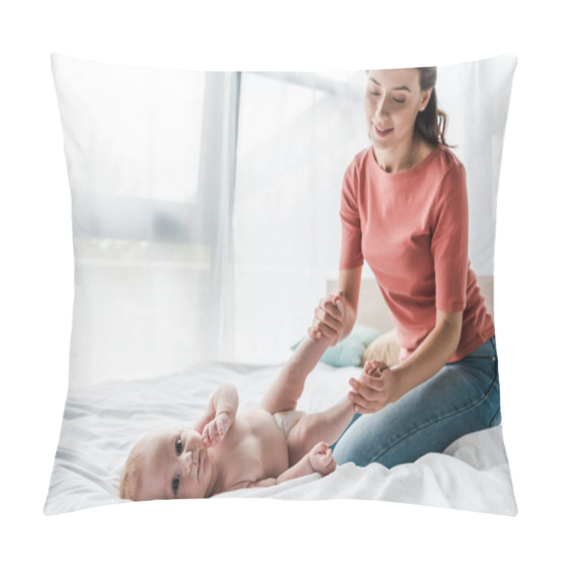 Personality  happy mother touching legs of baby lying on bed  pillow covers