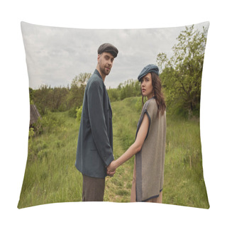 Personality  Fashionable Woman In Vest And Newsboy Cap Looking At Camera And Holding Hand Of Bearded Boyfriend In Jacket And Standing With Landscape And Overcast At Background, Stylish Couple In Rural Setting Pillow Covers