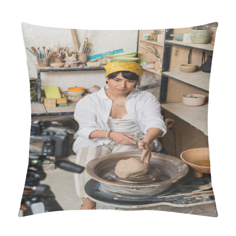 Personality  Young asian female artist in headscarf and workwear looking at digital camera while sitting near clay on pottery wheel in ceramic workshop at background, pottery artist showcasing craft pillow covers