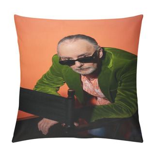 Personality  Serious And Confident Senior Man In Green Velour Blazer Looking At Camera Over Dark And Trendy Sunglasses While Posing Near Chair On Red And Orange Background, Fashionable Aging Concept Pillow Covers